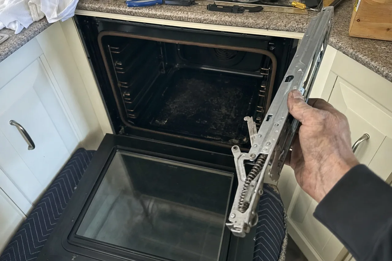 An oven door taken off and held by its hinge arm beside the open cavity